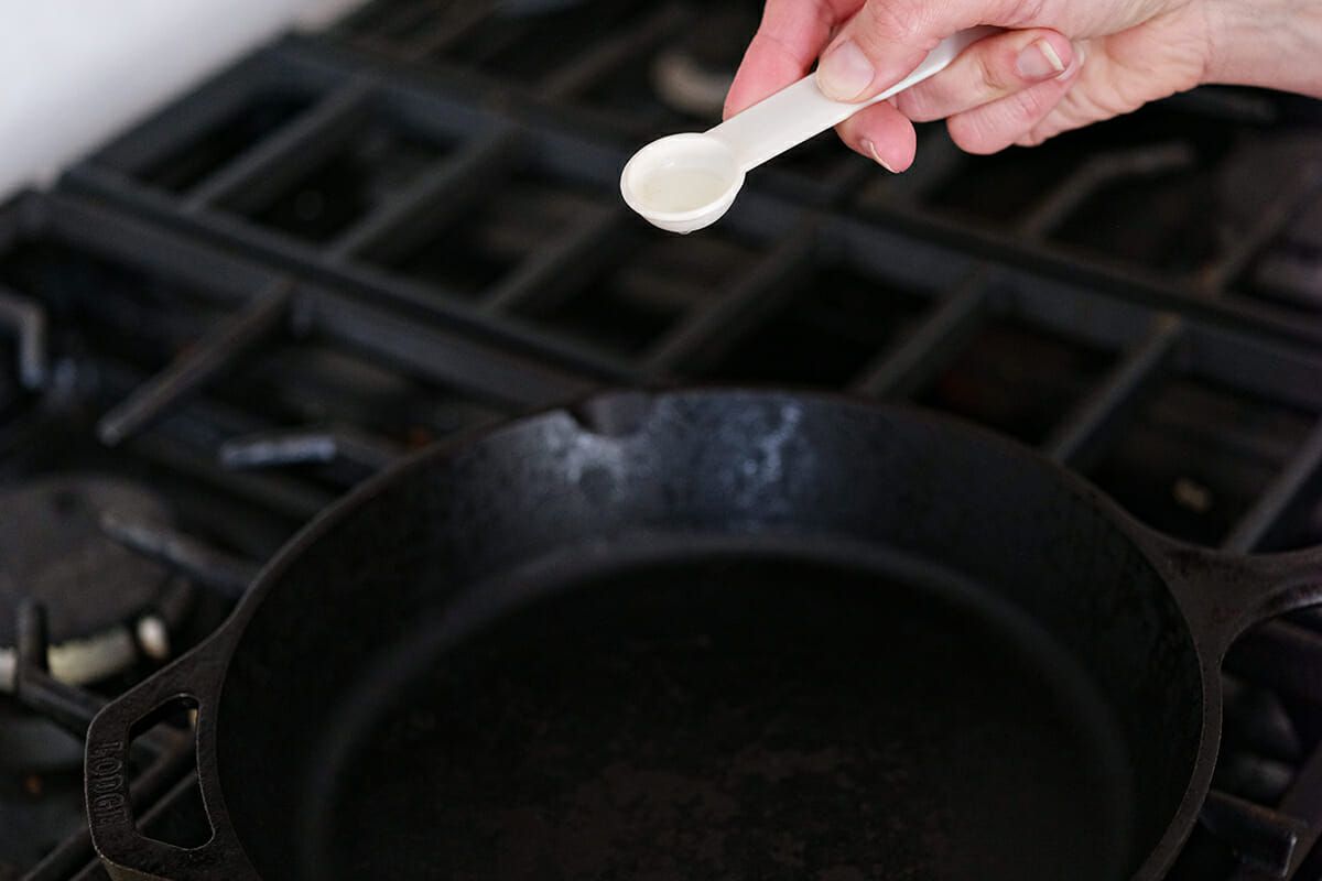 How to Clean Cast Iron - woman pouring oil into a cast iron skillet on stove