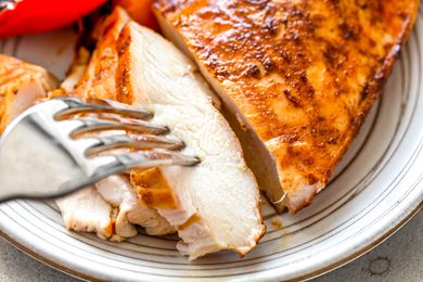 A fork tucking into slices of grilled chicken breast on a plate