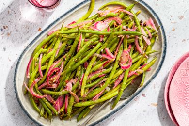 pickled green beans on a platter next to a glass of water and a stack of plates