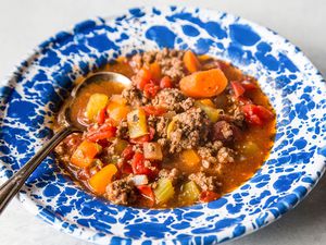 Hamburger soup with vegetables resting in a blue bowl 