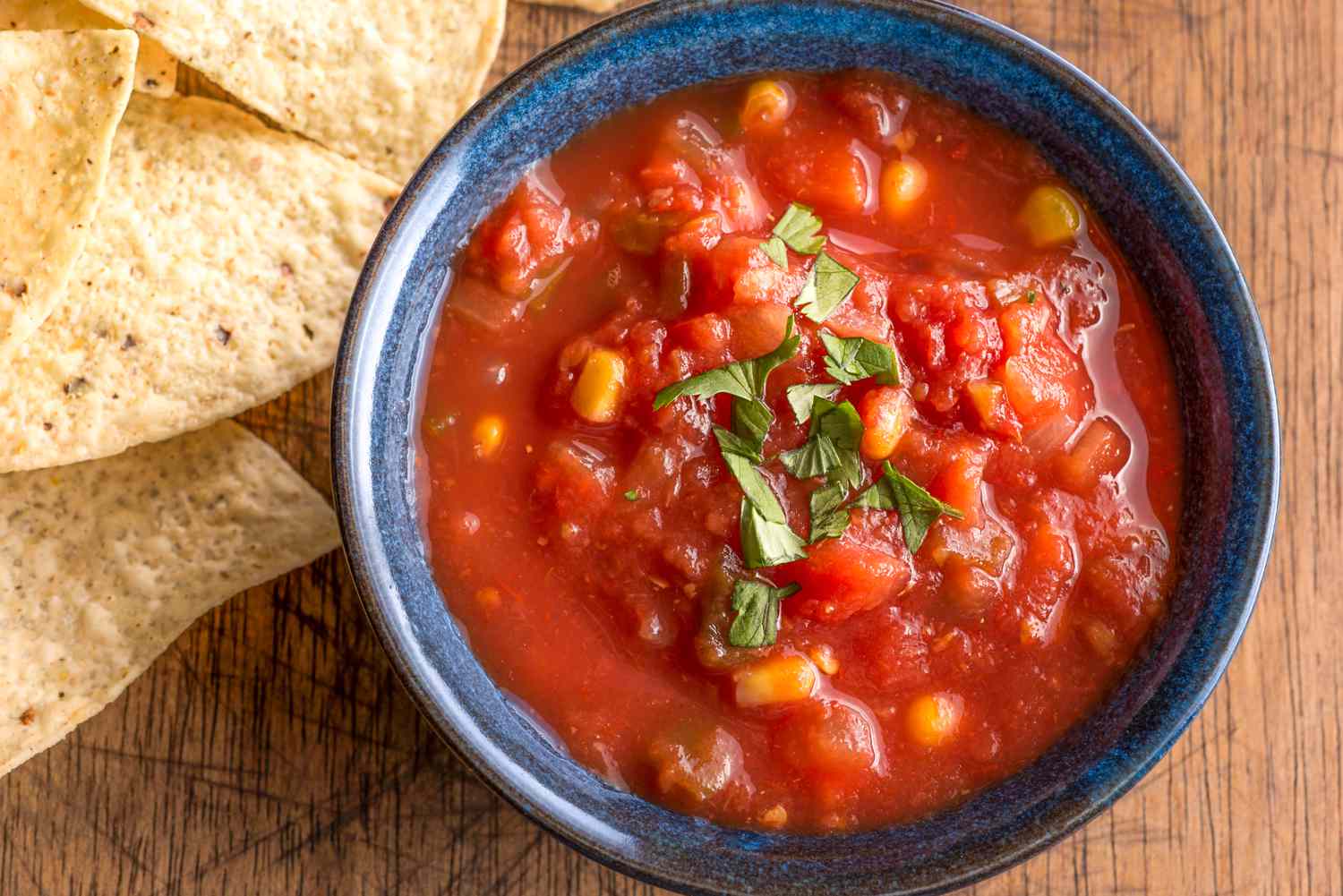 A blue bowl filled with salsa, with tortilla chips on the side