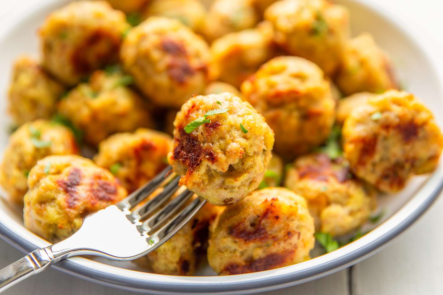 Closeup view of a fork holding a 3-ingredient chicken meatball in front of a bowl of more meatballs in the background
