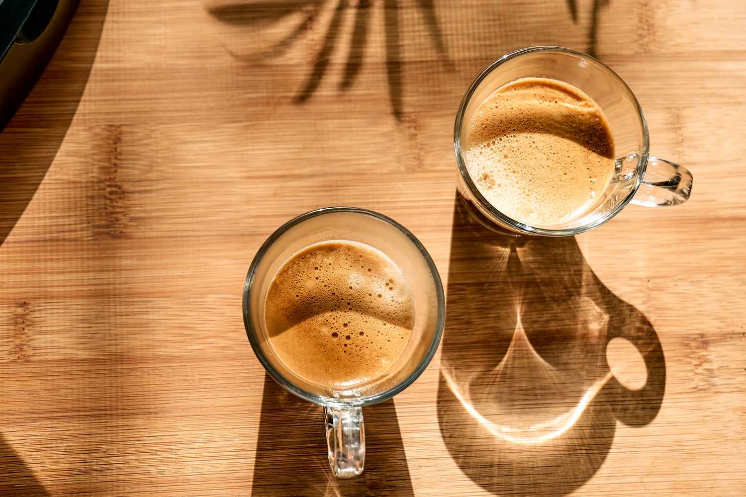 Overhead shot of two glass cups of coffee on a wooden counter top