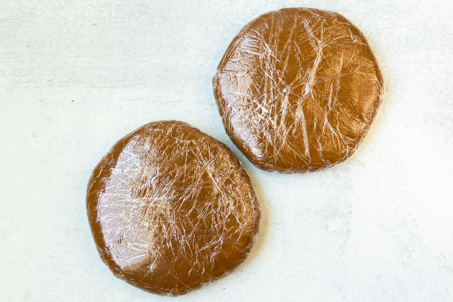 Two dough rounds in plastic wrap for a gingerbread house recipe.