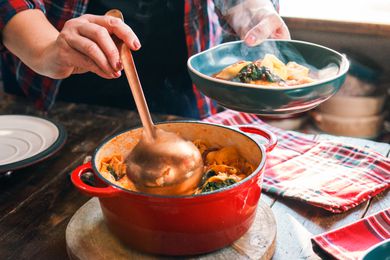 Someone serving soup with a ladle from a Dutch oven to a blue bowl