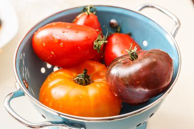 A blue colander containing various fresh tomatoes