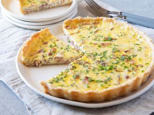 Quiche lorraine with a piece set on a plate behind it.