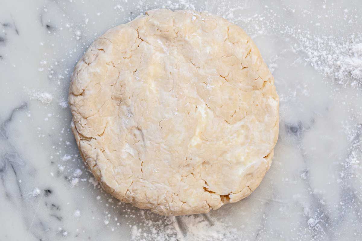 A disk of homemade quiche dough is sprinkled with flour and is on a marble countertop.