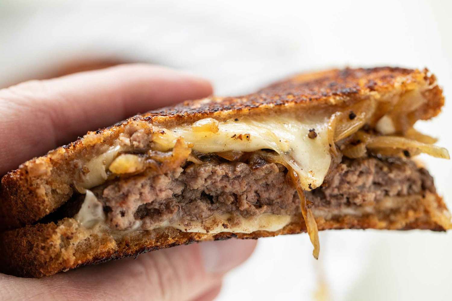 Perfect patty melt held in a hand with the melted cheese, caramelized onions and beef patties visible.