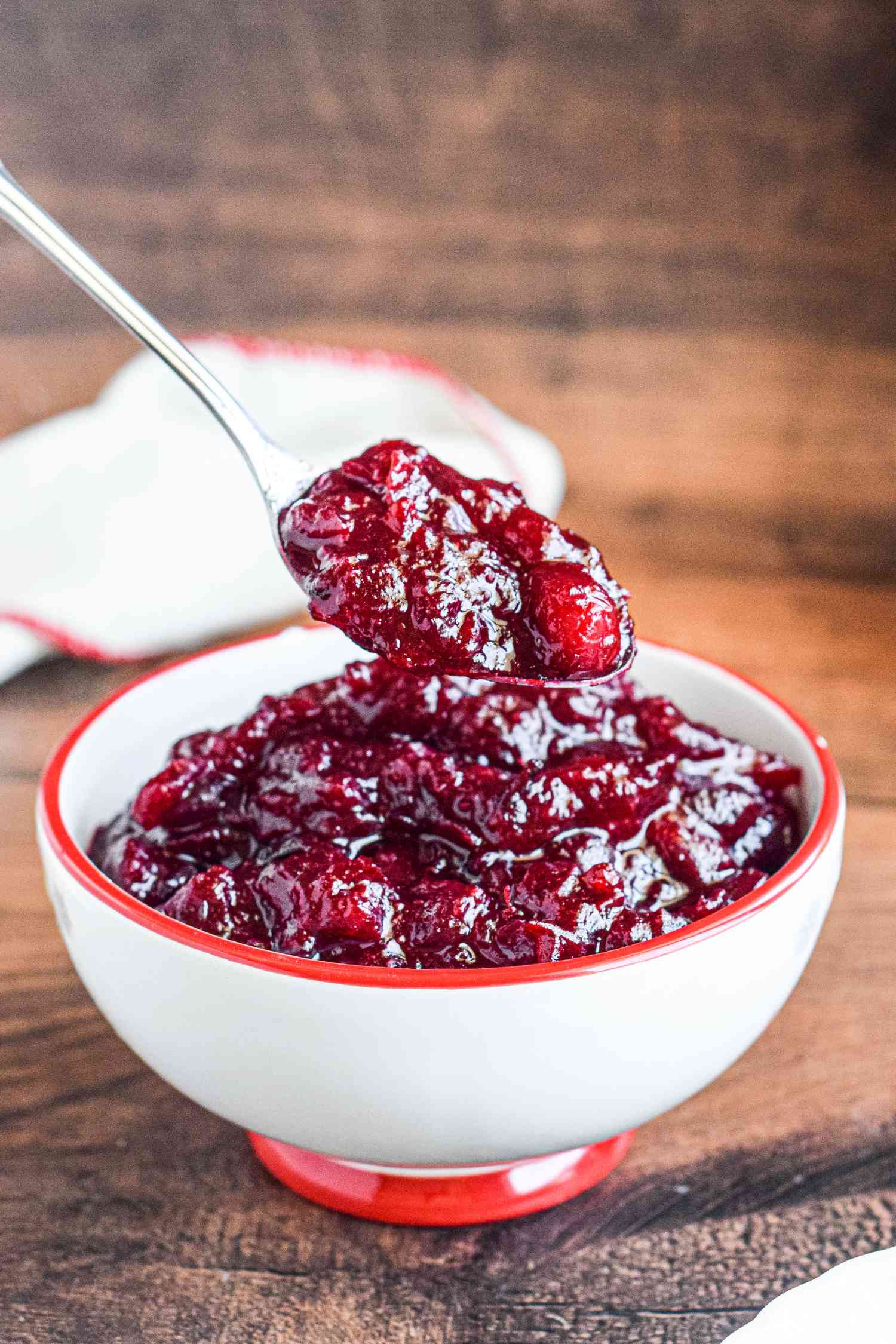 A bowl of cranberry sauce on a table with a spoon.
