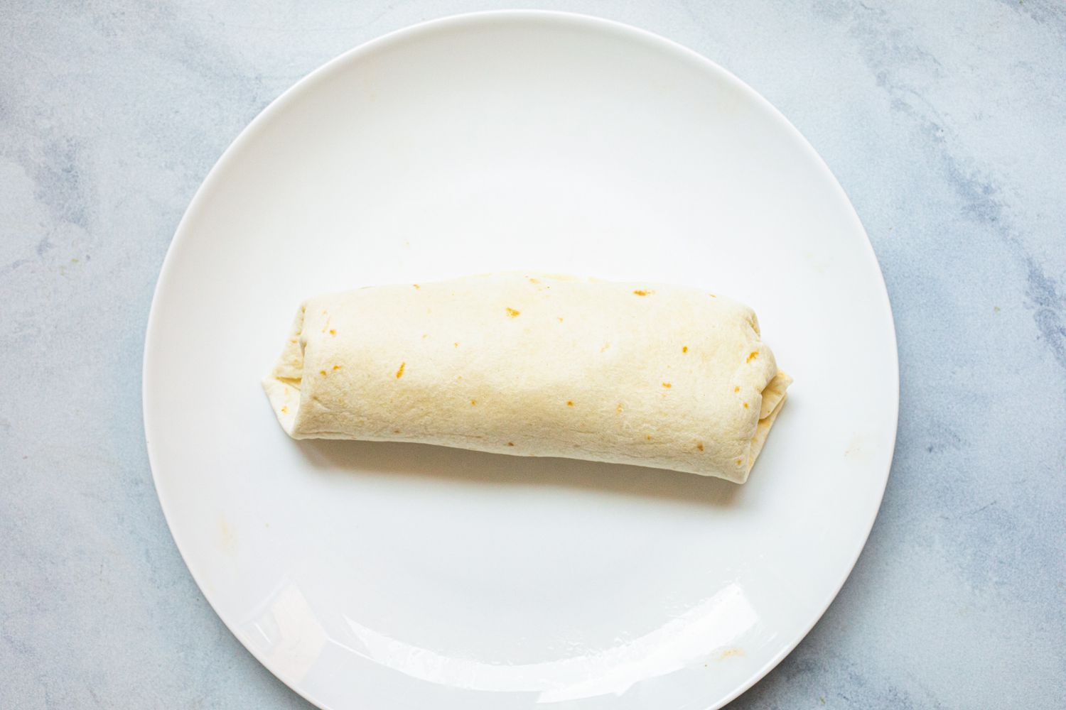 Veggie burrito with beans, corn, and peppers on a white plate.