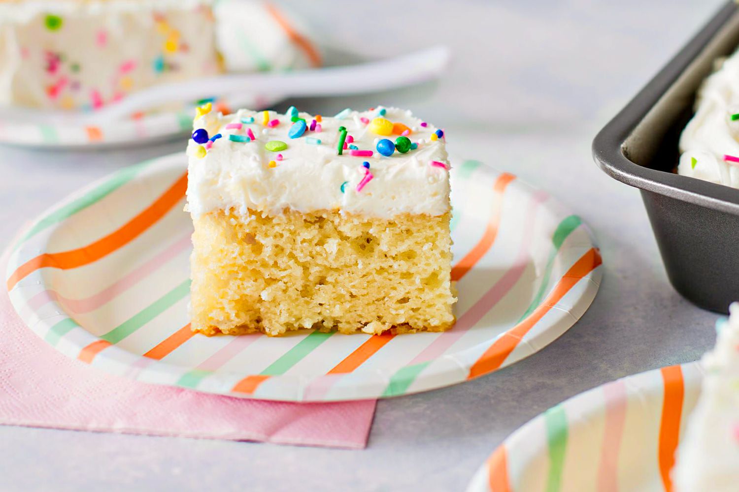 slice of vanilla cake on a paper plate a table with more slices on other paper plates 