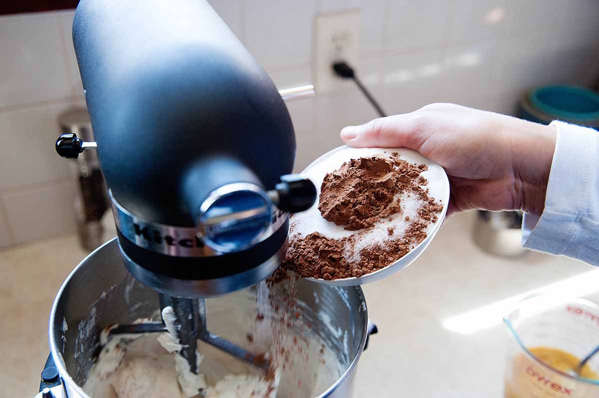Adding coco powder to a mixing bowl with creamcheese to make homemade chocolate cheesecake.