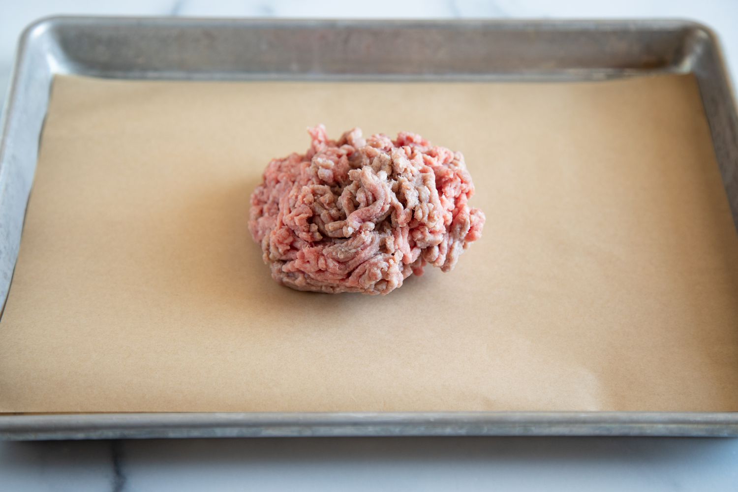 Mound of raw ground beef in the middle of a baking sheet lined with parchment paper