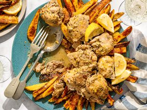 A dish of braised chicken served on a plate with fries and lemon wedges