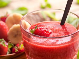 A strawberry smoothie in a glass with a straw and fresh strawberries around