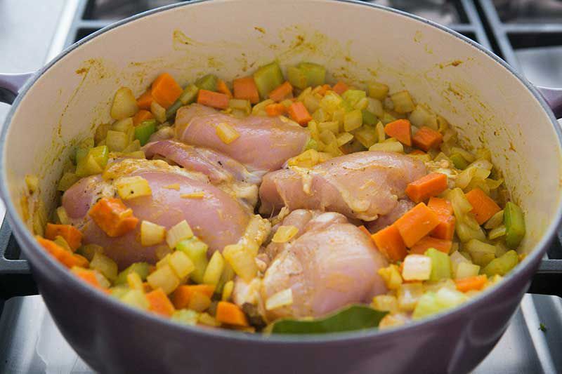 Chicken thighs on top of onions, carrots, celery in a Dutch oven