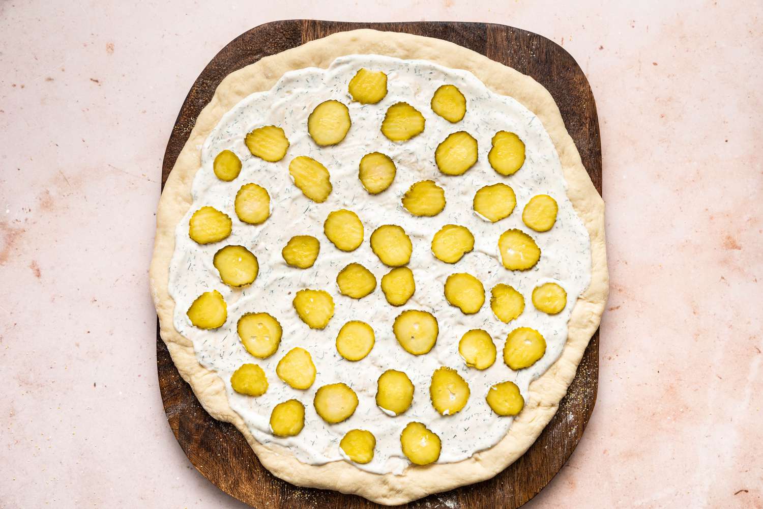 adding pickles to an unbaked pickle pizza