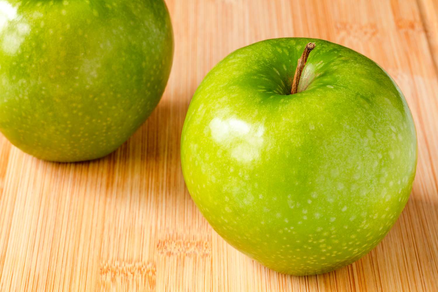 Close up of two Granny Smith apples on a bamboo cutting board
