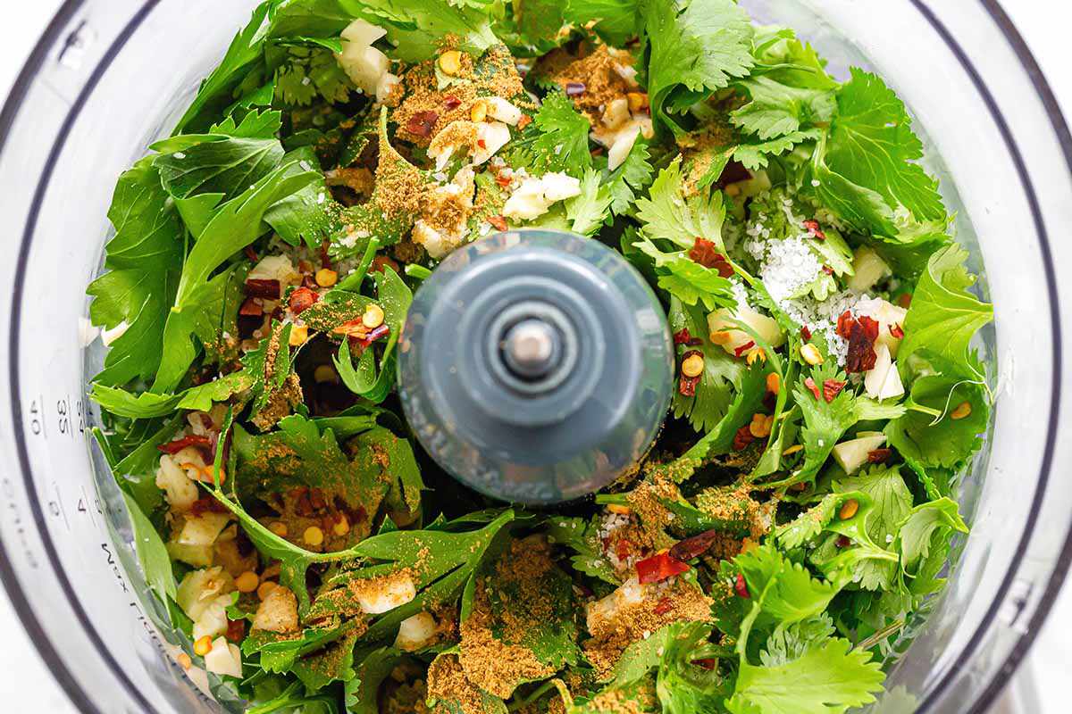 Herbs, spices and oils mixed together in a food processor to make chimichurri with avocados for skirt steak