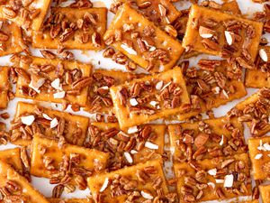 Overhead shot of club cracker cookies topped with chopped mixed nuts spread out on a white surface