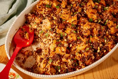 Greek-style stuffing in an oval white serving dish, with a red serving spoon in the right corner where some of the stuffing has been scooped out