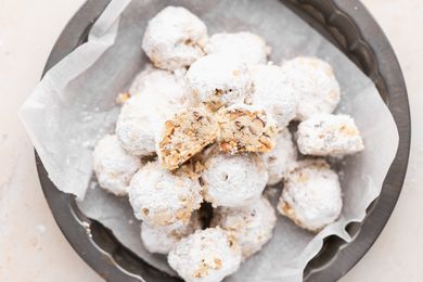 Overhead view of powdered sugar cookies piled on a plate with the top one cut in half to show the interior.