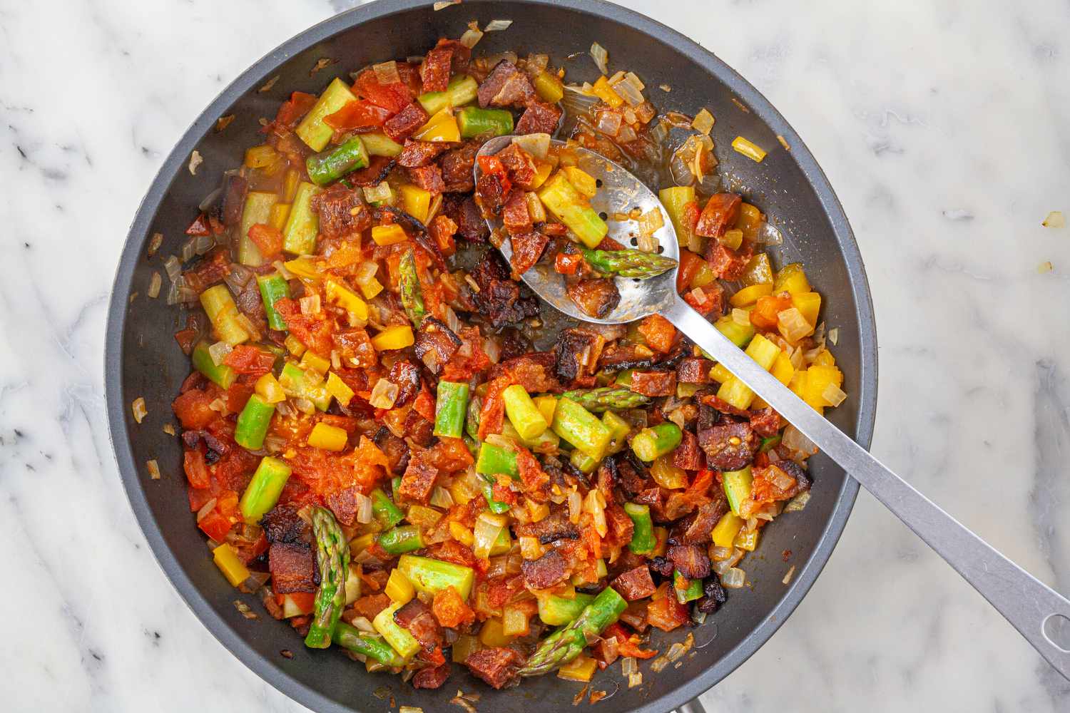Spanish Style Migas with Asparagus, Chorizo, Bacon, and Eggs in a skillet.