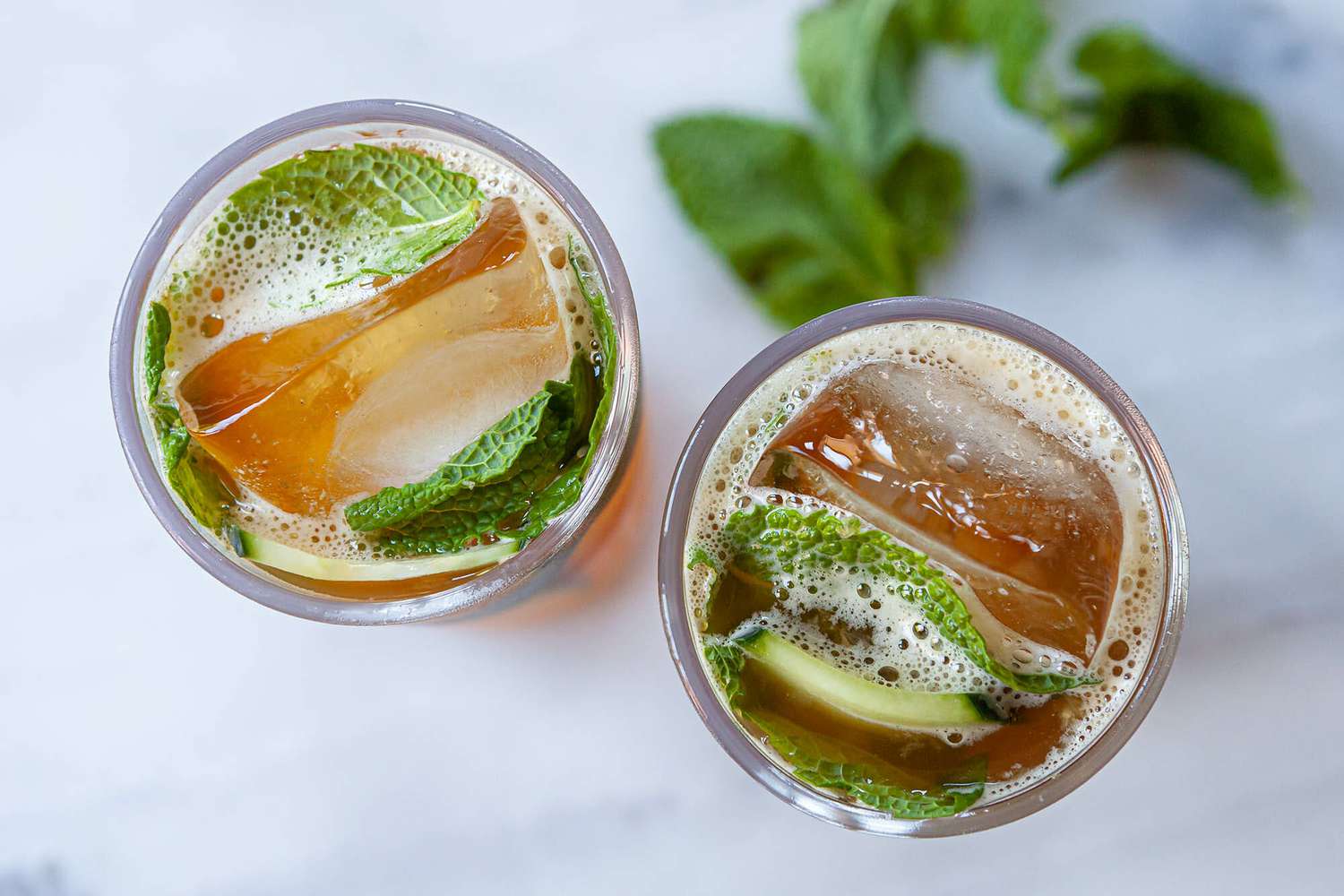 Overhead view of New orleans Pimm's cup cocktail in highball glasses. Ice, cucumber and mint are visible in the glasses.