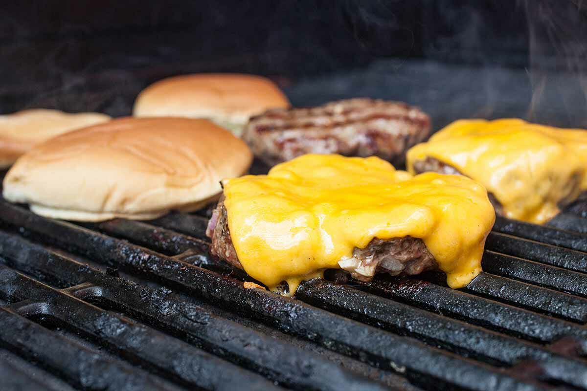 Melting cheese on burger with buns on grill