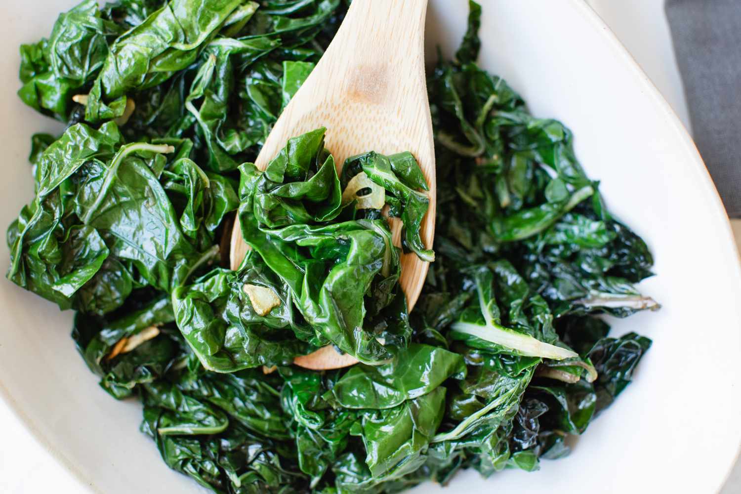 Wooden spoon scooping up cooked spinach recipe.