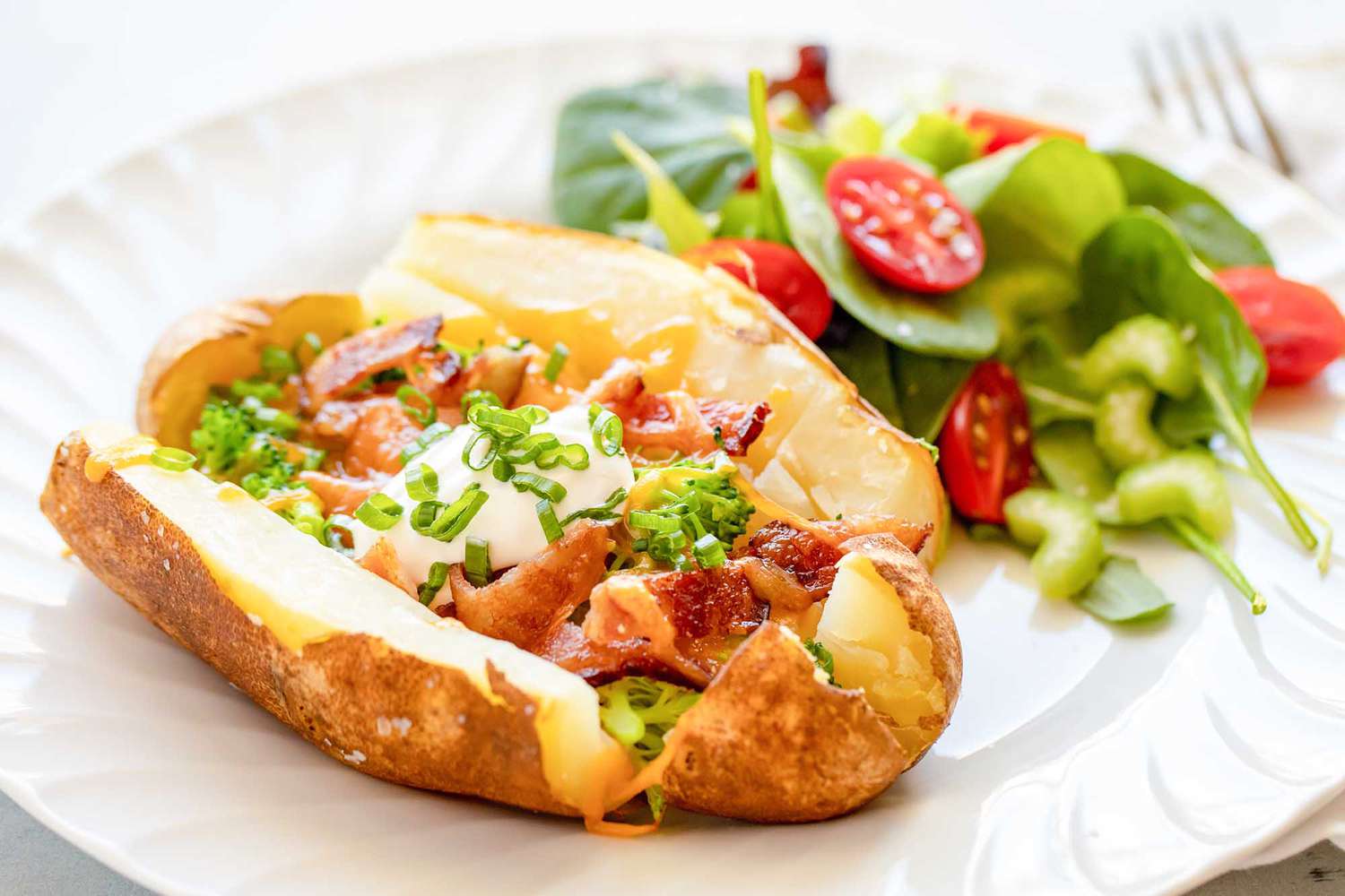 loaded baked potato with bacon, broccoli and sour cream with a side salad