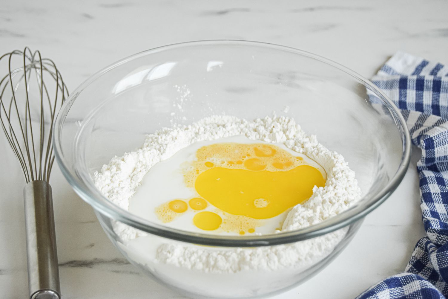 A glass bowl and whisk with ingredients to make a yorkshire pudding recipe.
