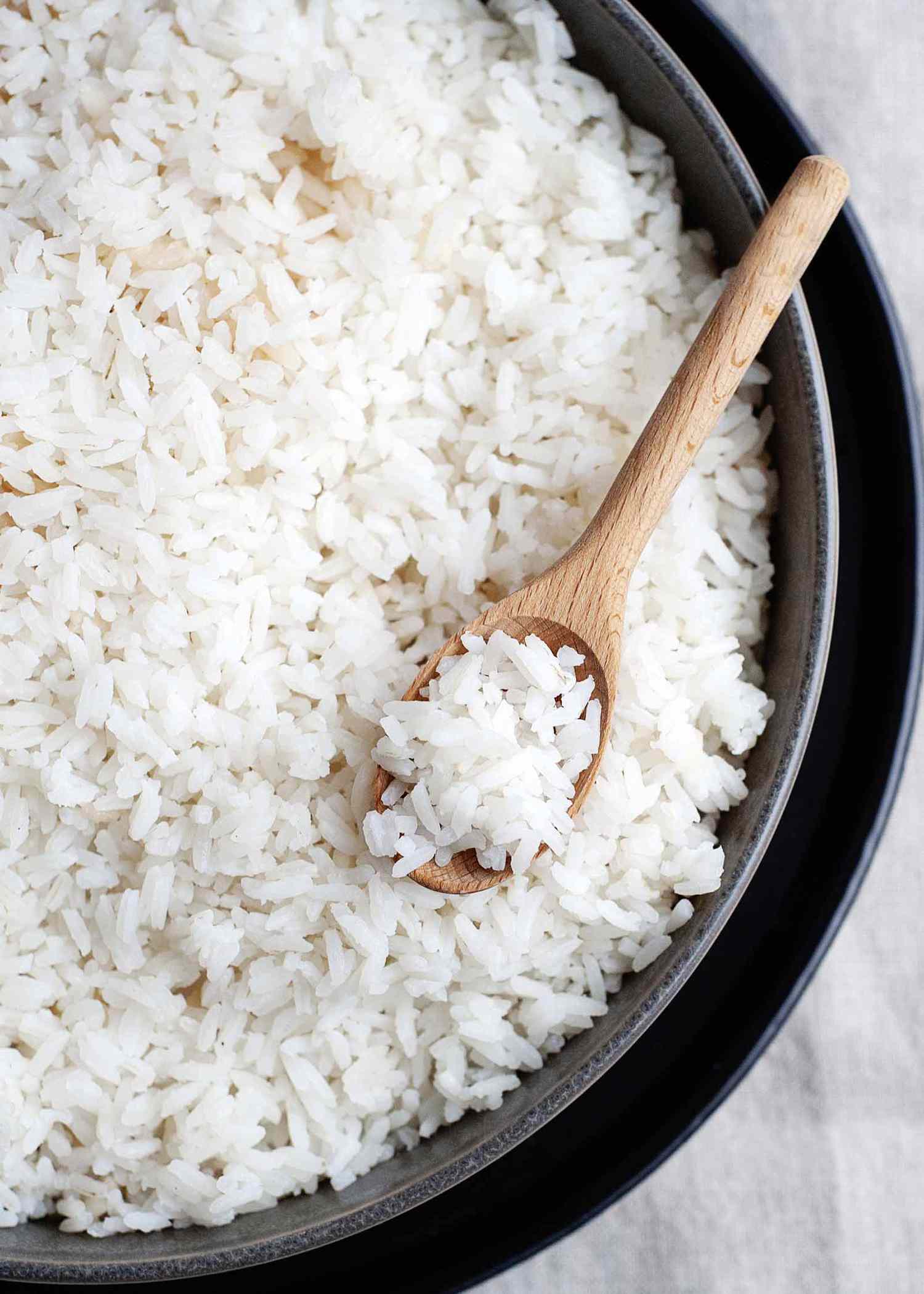 Easy white rice in a metal pan sitting in a deep tray with a wooden spoon full of rice inside.