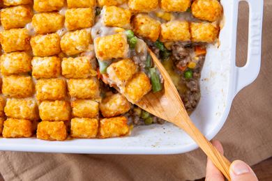 hand with wooden spoon scooping out some Classic Tater Tot Hotdish out of baking dish