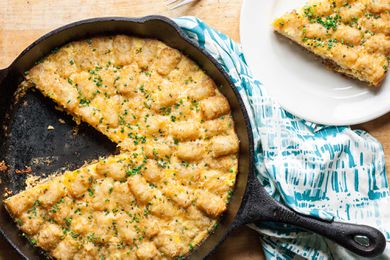 Tater Tot Breakfast Casserole in a cast iron skillet, one slice removed and placed on a dish