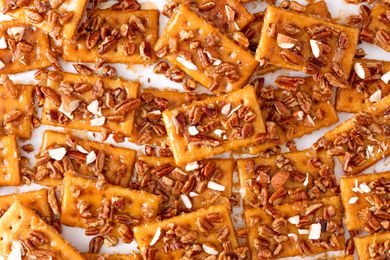 Overhead shot of club cracker cookies topped with chopped mixed nuts spread out on a white surface