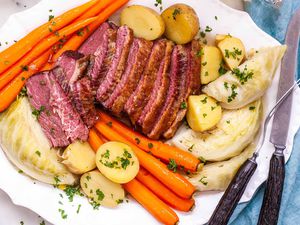 Best Boiled Corned Beef and Cabbage Recipe - platter of sliced corned beef, carrots, potatoes, and cabbage sprinkled with herbs