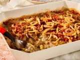 Angled view of a beige casserole dish with green bean casserole along with a serving spoon