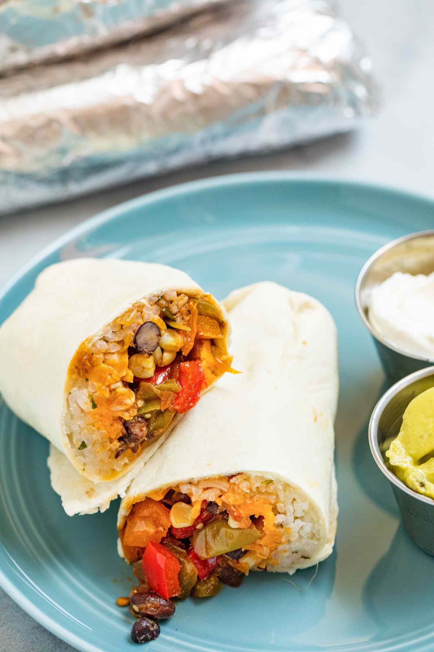 A plate of black bean, corn, and pepper freezer burritos with guacamole and sour cream on the side.