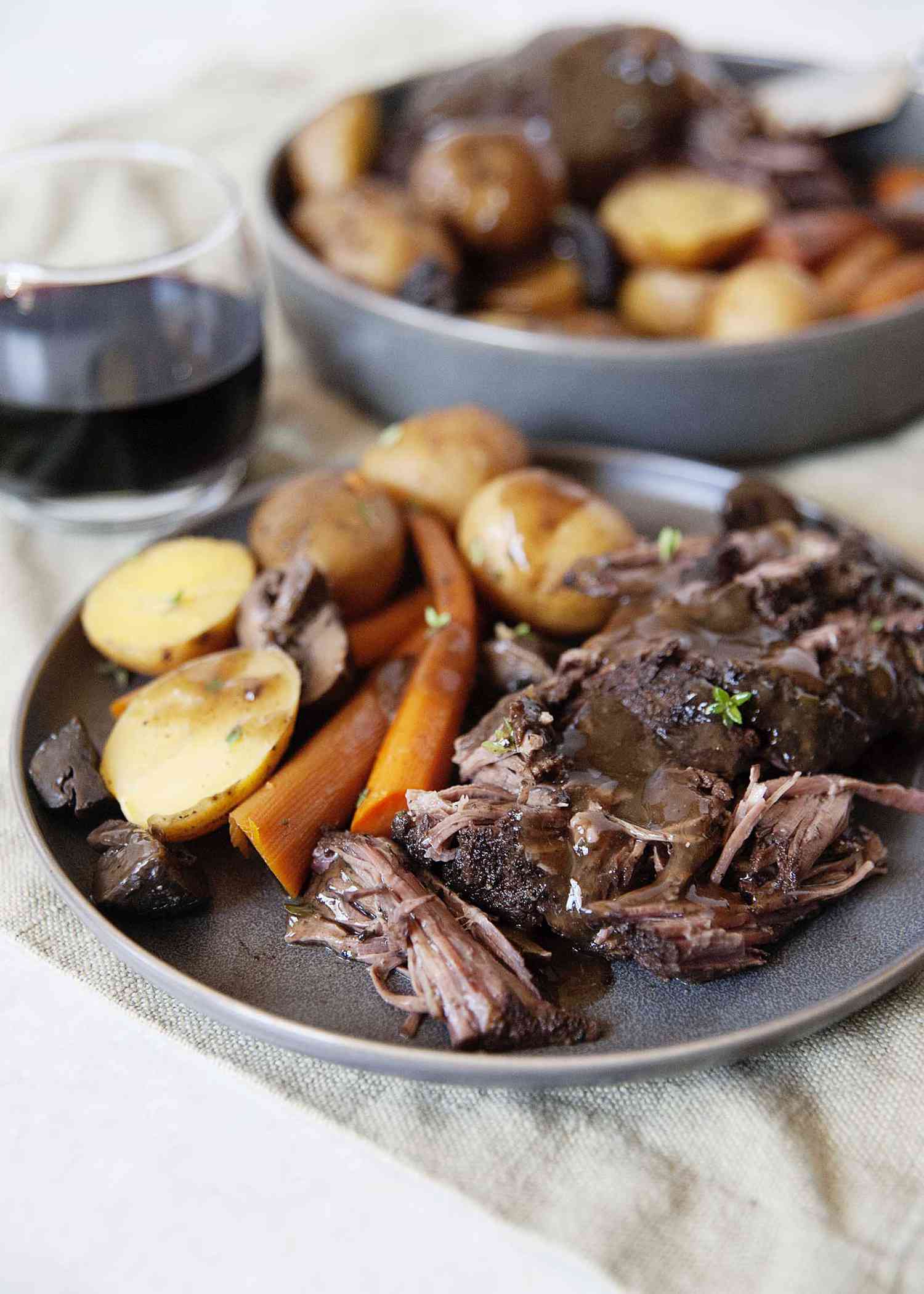 Side view of tender pot roast made in a slow cooker with gracy, cooked carrots and potatoes.