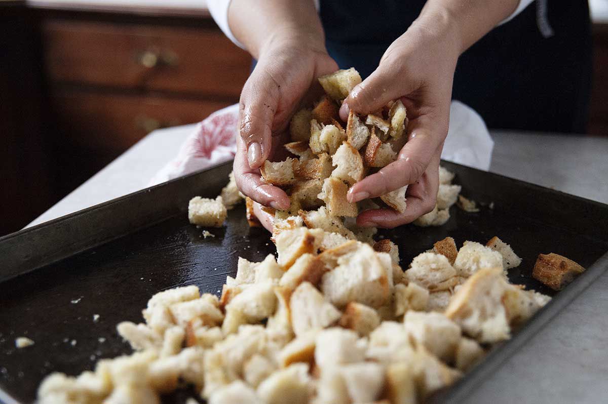 Woman tossing cubed bread on a baking sheet for thanksgiving stuffing.