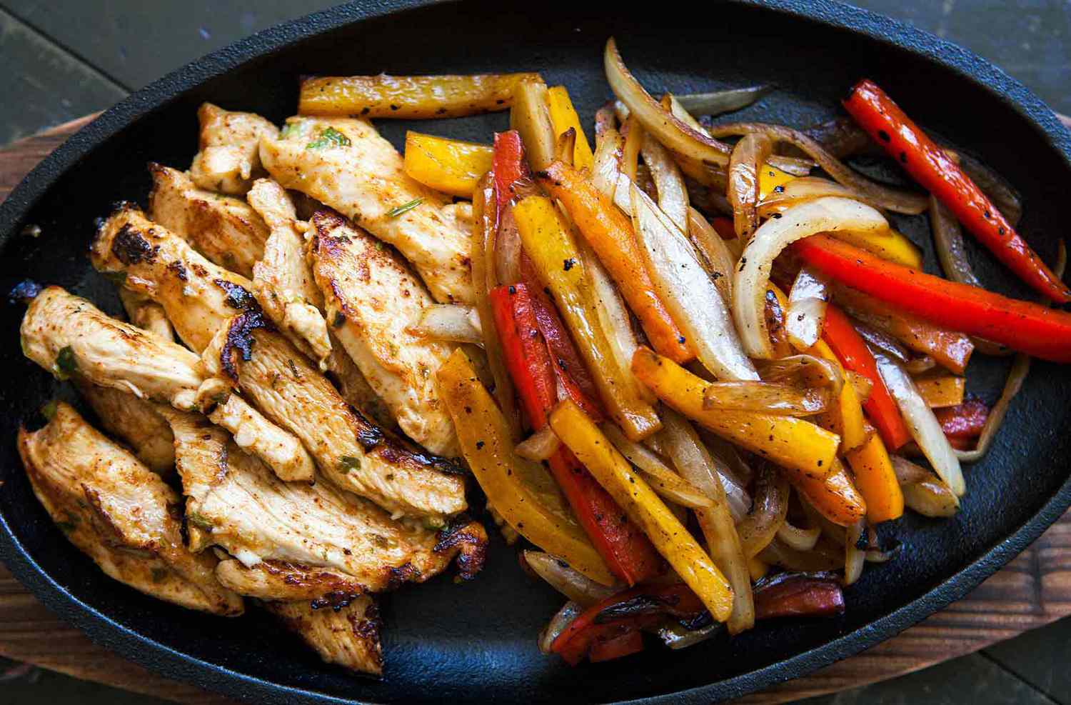 A cast iron platter with sliced chicken breast, onions and peppers ready to serve.