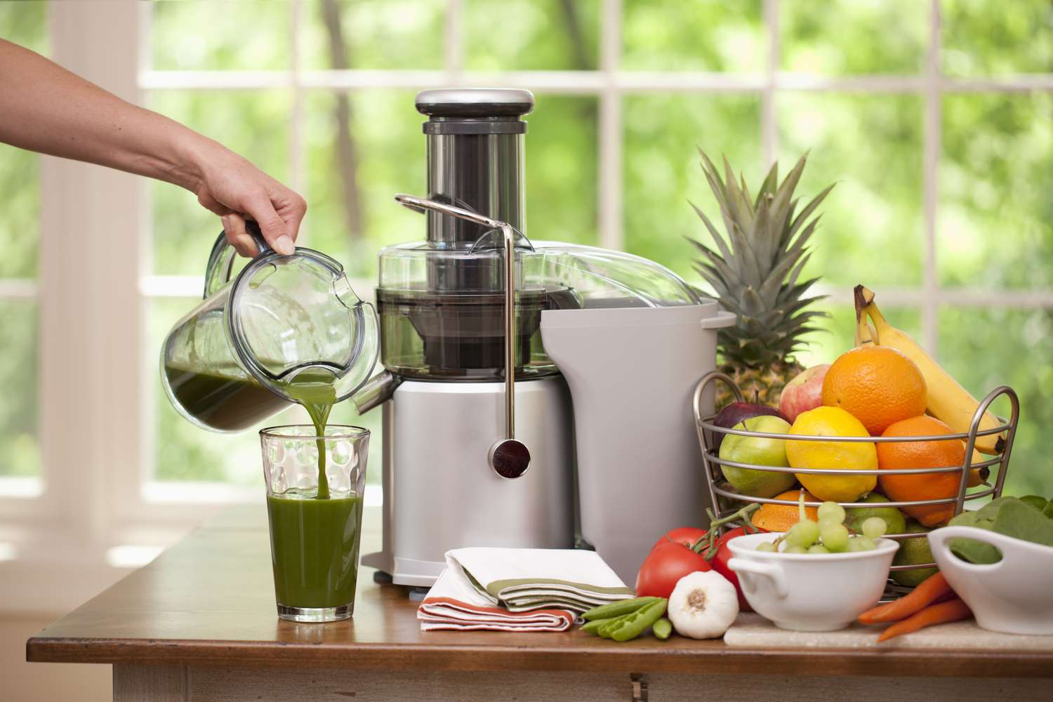 a juicer with fresh fruit and a hand pouring juice into a glass
