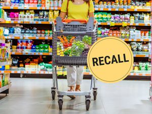 A woman wearing a bright yellow shirt pushing a shopping cart down a grocery store aisle.