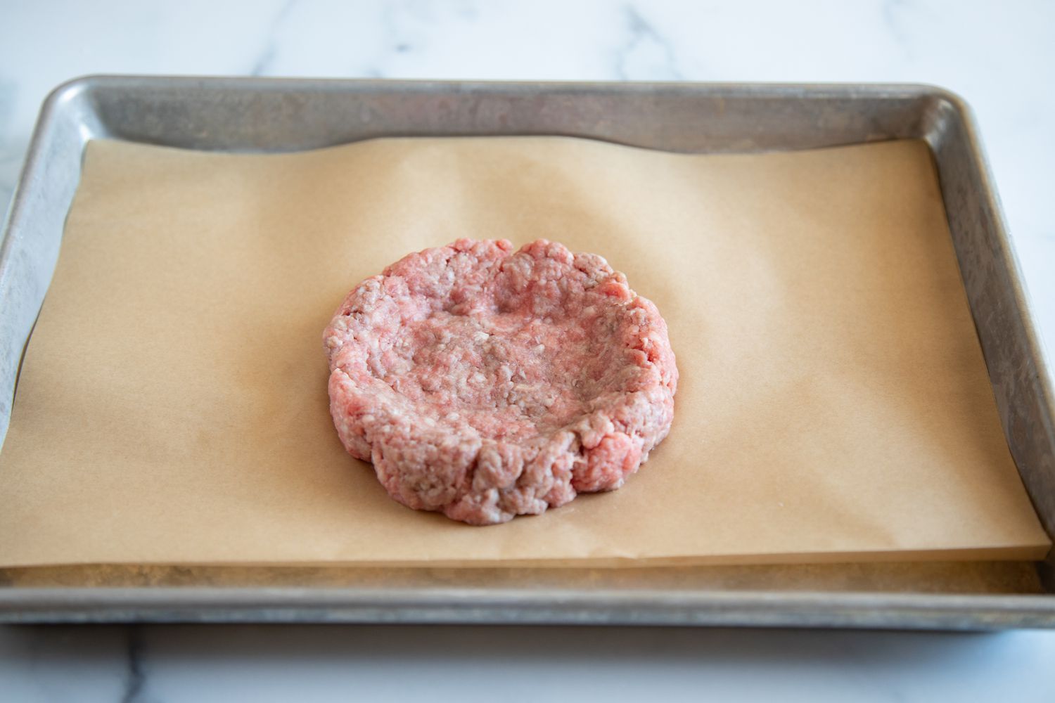 Dimpled raw ground beef patty on baking sheet
