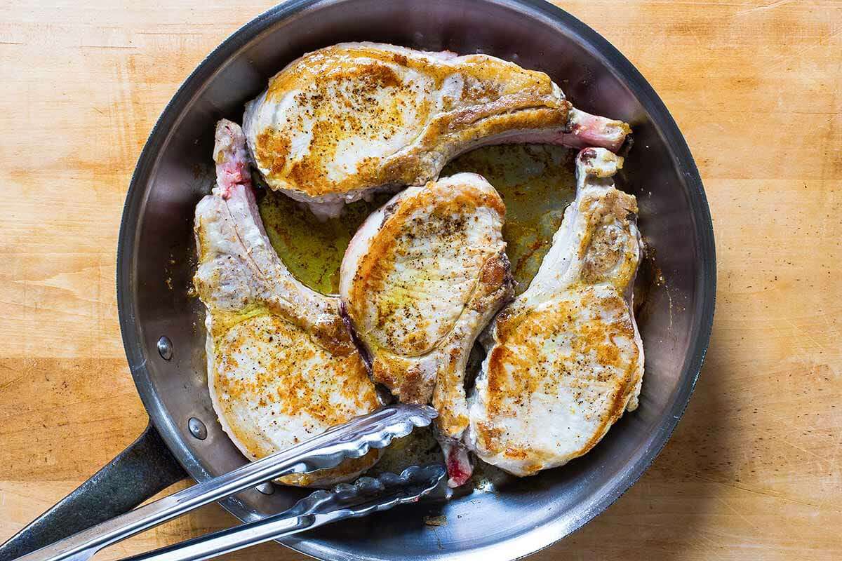 Pork loin chops being seared in a pan