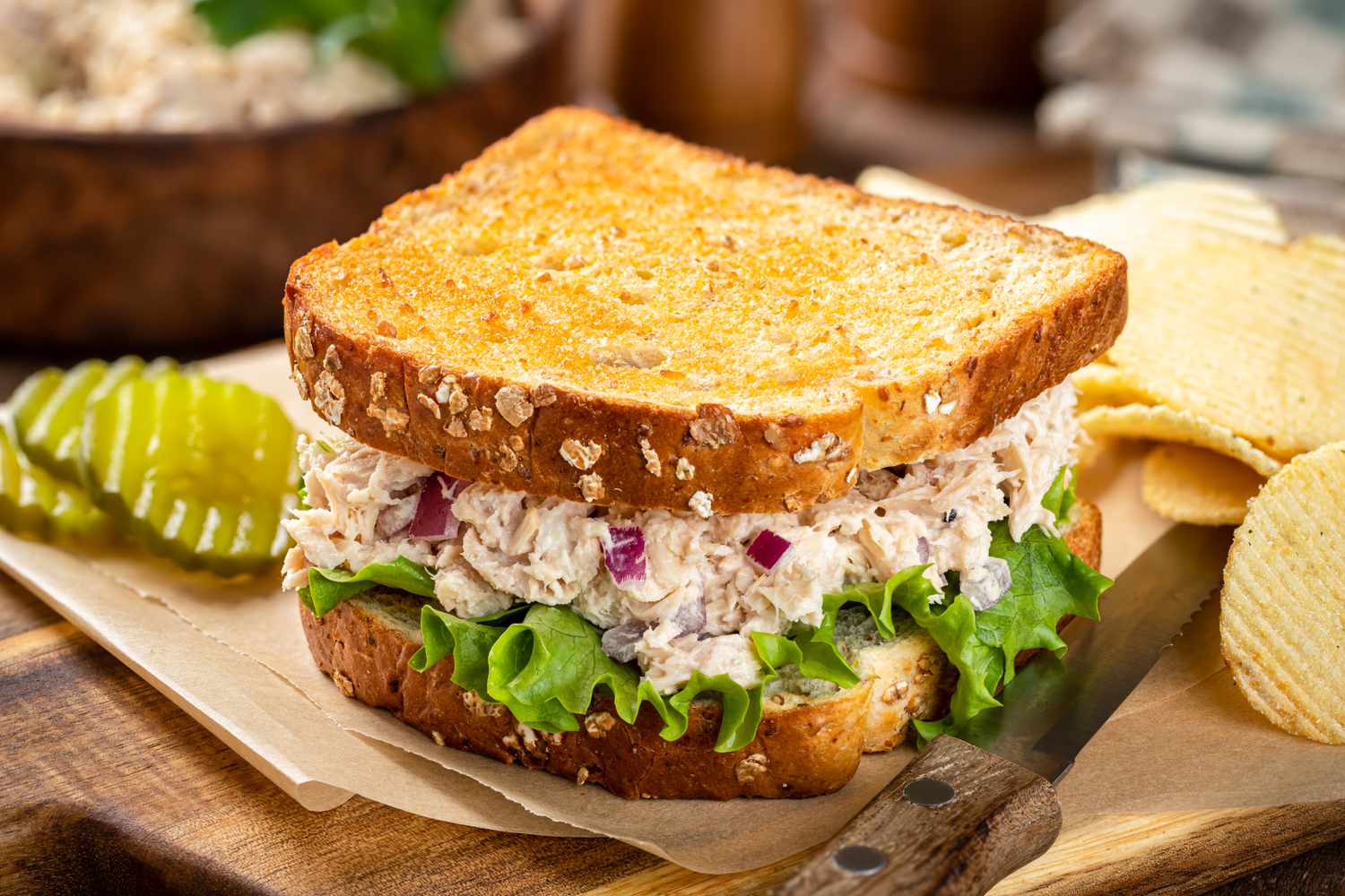 Tuna salad sandwich next to pickles and chips