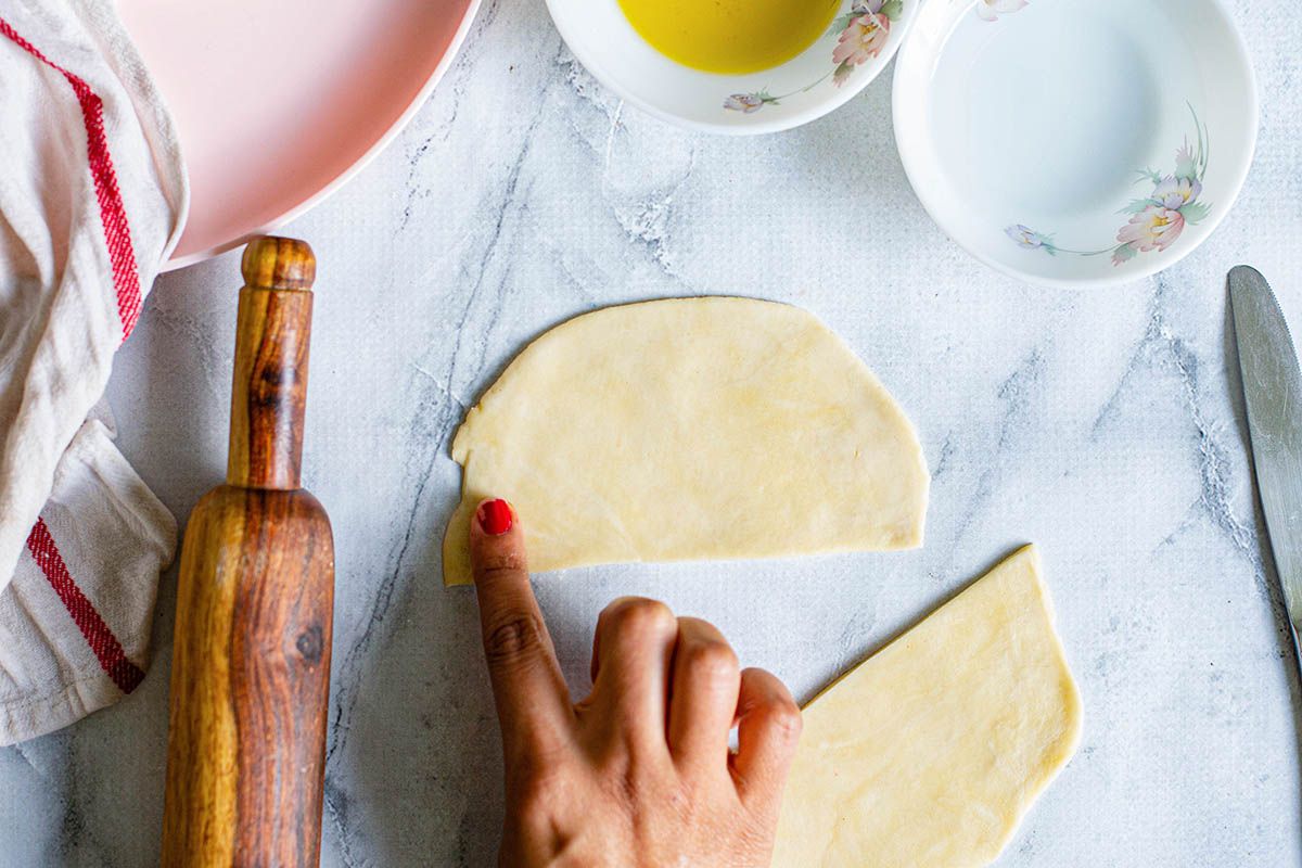 A circle of dough cut in half on a counterop with dishes and a rolling pin nearby.