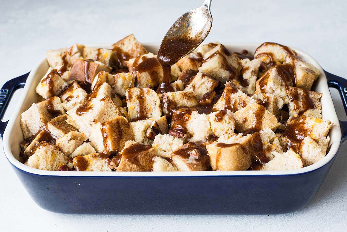 Bread cubes in a casserole dish being drizzled with a brown sugar mixture